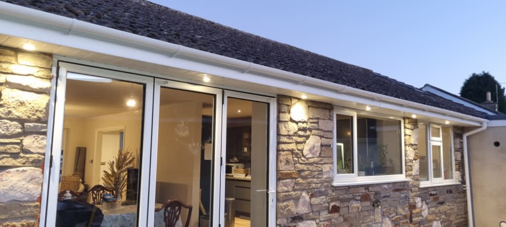 Recessed exterior lights illuminating a stone house and patio doors